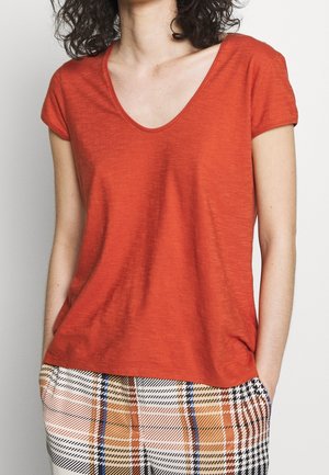 Rotes T-Shirt mit kurzen Ärmeln und V-Ausschnitt, aus einem strukturierten Stoff gefertigt, kombiniert mit einer Hose aus Karomuster mit orangefarbenen und blauen Akzenten.