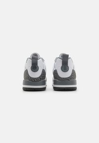 Chaussures de sport blanches avec un talon texturé gris, des accents gris assortis et un logo rond à l'arrière. Elles présentent une semelle grise robuste.