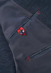 Navy jacket section with zippered pockets featuring red accents and button. Material shows textured pattern with stitching detail.