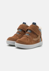 Des chaussures montantes en suède brun avec des accents bleus, dotées de deux bandes Velcro, d'un doublure intérieure rembourrée et d'une semelle en caoutchouc blanc texturé.