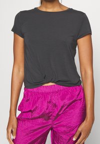 Camiseta negra de manga corta con detalle anudado en el frente, combinada con pantalones texturizados fucsias brillantes que cuentan con una cinturilla elástica.