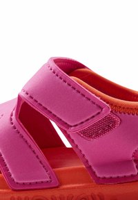 Růžové syntetické sandály mají nastavitelné popruhy, texturované uzavírání na suchý zip a oranžovou polstrovanou vnitřní část s plochou gumovou podrážkou.