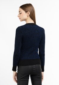 Maglione lavorato a maglia nero e blu con un motivo testurizzato, maniche lunghe e orlo a coste. Abbinato a pantaloni neri aderenti.