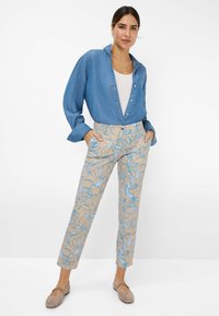 Lichtdenim knoopshirt, witte tanktop, beige broek met blauw bloemenpatroon en beige flats, met een relaxte pasvorm en zakken.