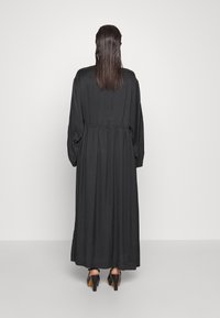 Lang schwarz Kleid mit langen Ärmeln und einem elastischen Taillenbund, aus einem glatten Material gefertigt. Der Rücken ist schlicht, mit einem bodenlangen Design.