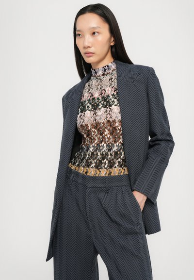 Blazer scuro navy su misura con un motivo a spina di pesce, abbinato a un top testurizzato multicolore con intricate decorazioni floreali.
