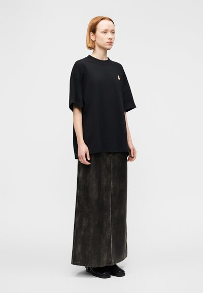 Μαύρο υπερμεγέθες T-shirt με κοντά μανίκια, διακοσμημένο με μικρό κεντητό σχέδιο, συνδυασμένο με μακριά, σκούρα, υφασμάτινη φούστα denim με υφή. Μαύρα παπούτσια.