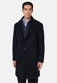 Tumesinine villasegu mantli, millel on üksnuppuline kinnitis, sälkklapid ja struktuurne sisekiht koos püsti kraega.