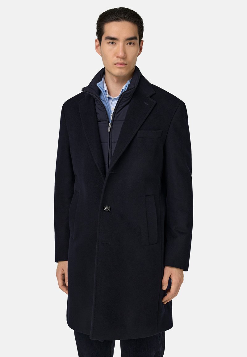 Tumesinine villasegu mantli, millel on üksnuppuline kinnitis, sälkklapid ja struktuurne sisekiht koos püsti kraega.