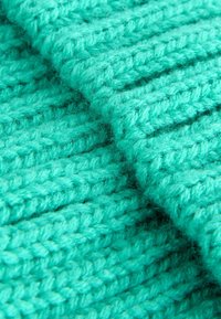 Gros plan d'un tissu en tricot teal montrant de grosses mailles avec un motif texturé de côtes verticales et diagonales.