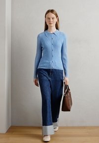 Cardigan côtelé bleu clair avec un col et un devant à boutons. Associé à un jean évasé bleu foncé avec des poignets en denim clair et des chaussures beiges. Sac marron.
