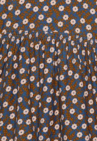 Tessuto di cotone floreale con sfondo blu, caratterizzato da fiori bianchi e foglie marroni. Dettaglio di cucitura arricciata lungo la linea orizzontale.