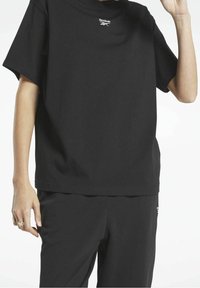 Svart bomullströja med avslappnad passform, med en liten vit Reebok-logga på bröstet. Slät textur, rund halsringning och korta ärmar.