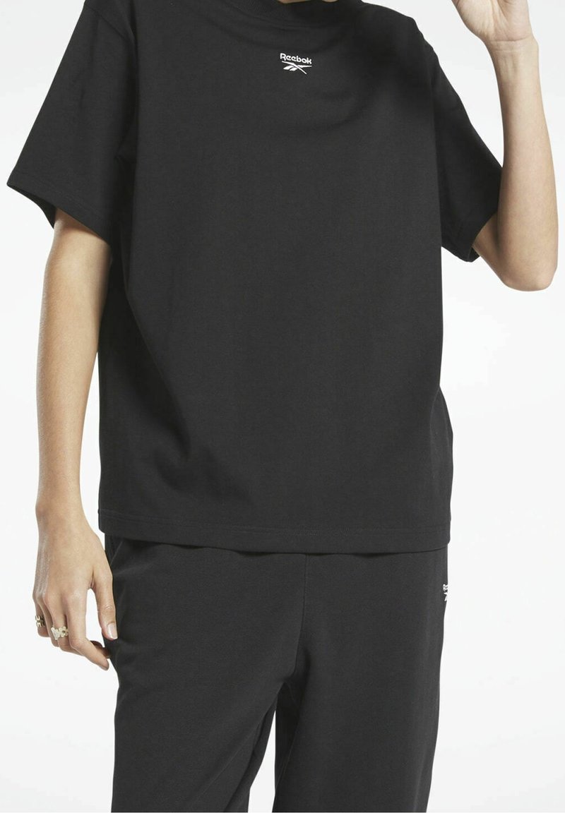 Svart bomullströja med avslappnad passform, med en liten vit Reebok-logga på bröstet. Slät textur, rund halsringning och korta ärmar.
