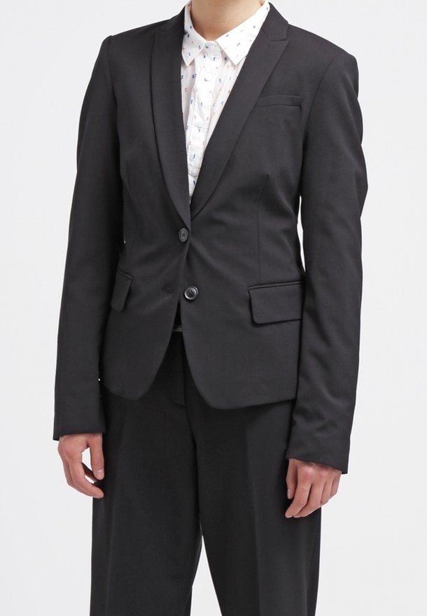 Černý přizpůsobený blazer se dvěma knoflíky, klopovými límci a klopovými kapsami. Nositý přes košili s límečkem a jemným vzorem. Hladká textura látky.