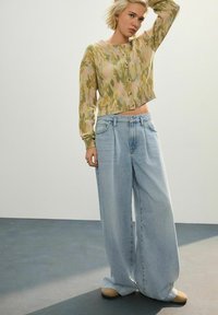 Cardigan tricotat cu un model de camuflaj verde și roz, asortat cu blugi light blue cu picioare largi. Croială supradimensionată, manșete cu nervuri și nasturi.