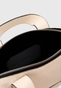 Crèmekleurige leren handtas met een zwarte binnenkant, voorzien van een ritssluiting en een gestructureerd oppervlak. Inclusief een klein zwart label aan de binnenkant.