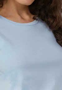 Lichtblauw katoenen T-shirt met een ronde halslijn. De stof lijkt zacht met een gladde textuur en minimale naden. Geen zichtbare patronen of accenten.