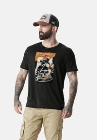 T-shirt noir avec un graphique de moto vintage en orange, bleu et blanc. Manches courtes, col rond et coupe décontractée visibles.