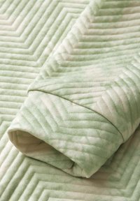 Textilväv med ett vågigt, strukturerat mönster i ljusgrön och krämfärgad, med fina åsar i ett zigzag-mönster.