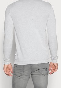 Chemise à manches longues gris clair avec un col arrondi, poignets ajustés et ourlet droit, associée à un jean slim gris avec poches arrière.