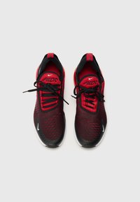 Ténis atléticos em vermelho e preto com uma parte superior em malha, padrão texturizado, biqueira arredondada e atacadores pretos. Logótipo da Nike em branco na lateral.