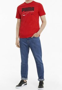 Rød bomulds T-shirt med et sort Puma-logo. Båret med blå jeans og sorte sneakers med hvide såler. Enkel crewneck-design.