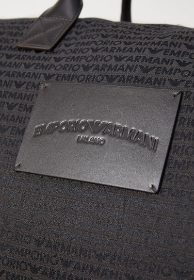 Sac en tissu noir avec un motif continu de logos "Emporio Armani", comportant une étiquette en cuir noir texturé embossée avec "Emporio Armani Milano."