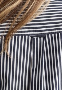 Navy and white striped fabric with a pleated design and a small sewn tab at the back. Smooth texture, cotton material.