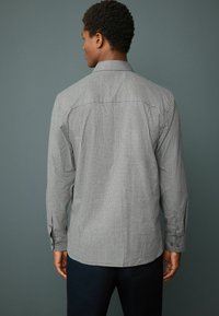 Gray checkered long-sleeve shirt featuring a button-down collar, with visible seams and button cuffs, paired with dark-colored trousers.