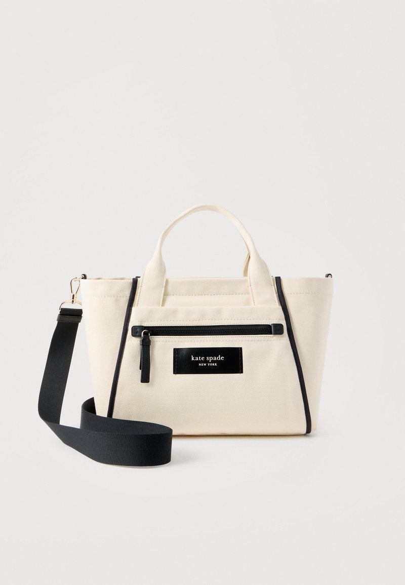 Τσάντα tote από κρεμ καμβά με μαύρη τσέπη με φερμουάρ και ρυθμιζόμενο μαύρο λουρί ώμου, με το λογότυπο "kate spade new york" στο μπροστινό μέρος.
