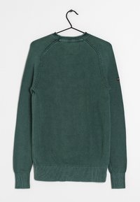 Pull en maille vert foncé avec un motif texturé, des poignets et un ourlet côtelés, et des manches raglan. Accroché à un crochet noir.