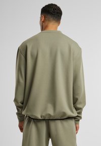 Sweat-shirt vert olive à coupe décontractée, col rond et ourlet élastiqué. Le matériau semble doux avec une texture lisse, aucun motif visible.