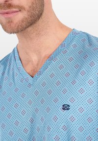 Maglietta blu a V con un motivo a pois rossi e blu navy, realizzata in tessuto traspirante con un logo ricamato sul petto.