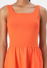 Ribbed orange sleeveless top with a square neckline, transitioning into a smooth, gathered fabric at the waist.