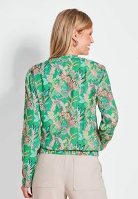 Groene bloemenprintjas met lange mouwen, elastische tailleband en subtiele textuur, met verschillende kleurrijke bloemen en bladeren.