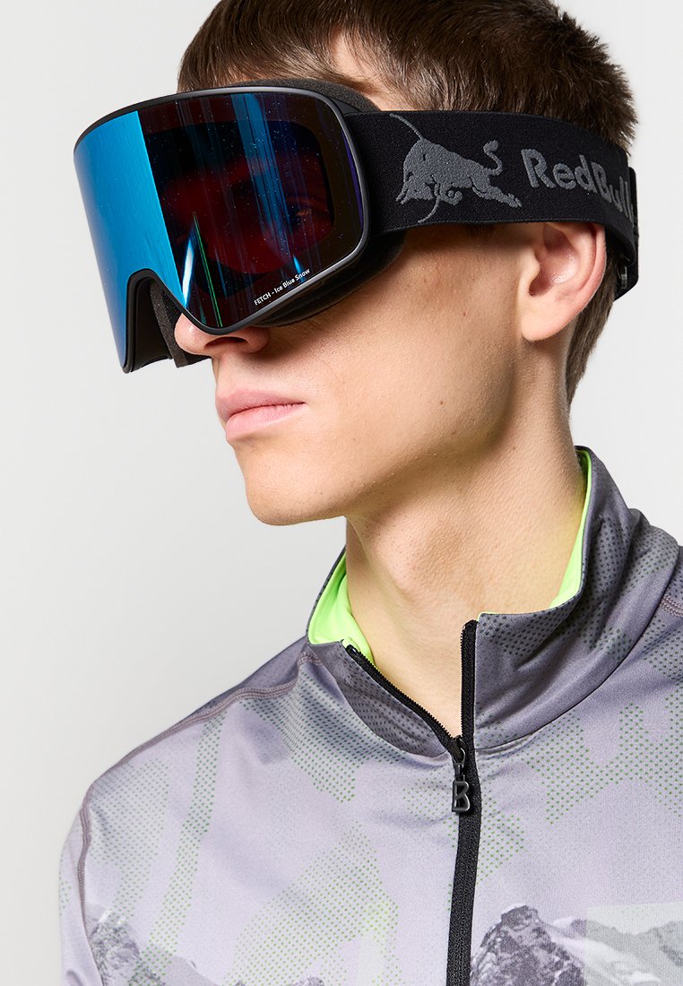Gogle narciarskie z czarną ramą, lustrzanym niebieskim szkłem i regulowanym czarnym paskiem z srebrnym logo, noszone z szaro-zieloną bluzą.