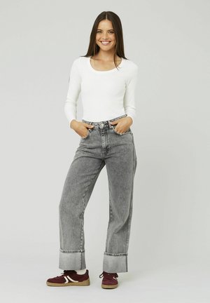 Haut à manches longues blanc associé à un jean large gris taille haute avec des ourlets retroussés et des baskets en daim bordeaux. Design et texture simples.