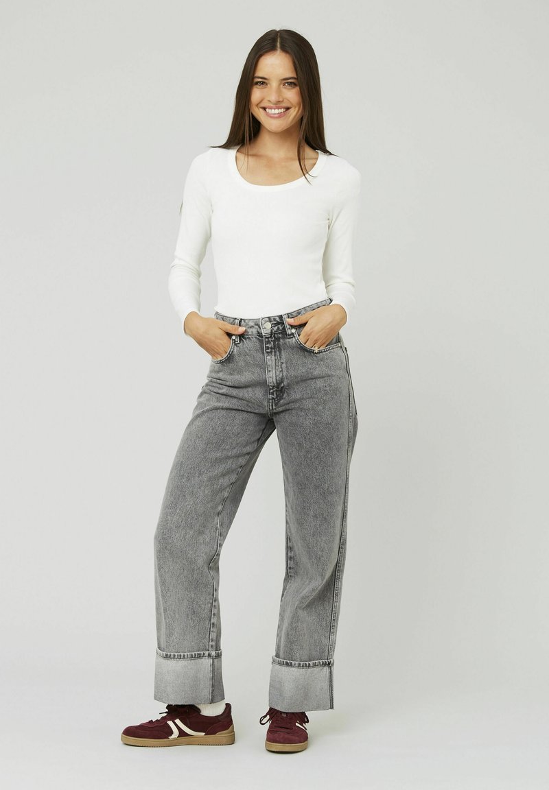 Haut à manches longues blanc associé à un jean large gris taille haute avec des ourlets retroussés et des baskets en daim bordeaux. Design et texture simples.