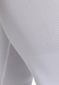 Leggings de sport blancs avec un motif en zigzag texturé, fabriqués à partir d'un tissu extensible, avec une finition lisse et un ajustement serré.