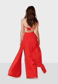 Vestido maxi rojo con un diseño sin tirantes y un lazo en la parte posterior, tejido fluido, altas aberturas y una textura suave.