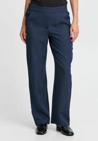 Pantalon rayé navy avec une taille élastique, coupe ample et texture lisse. Les chaussures assorties ont une finition brillante.