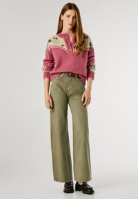 Suéter de punto en rosa con un canesú estampado; combinado con pantalones de pierna ancha en oliva y zapatos negros con detalles de tachuelas.