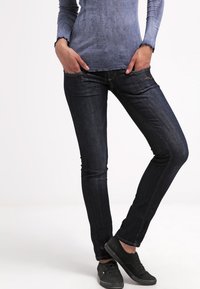 Jeans skinny de mezclilla oscura con una textura suave, que presentan bolsillos frontales y detalles de costura sutiles. Combinados con una blusa de manga larga con degradado.