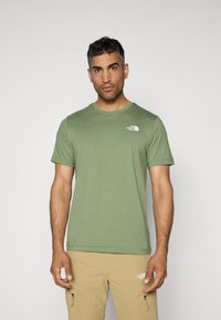 Camiseta de manga corta verde oliva con cuello redondo y un logo blanco en el pecho. Textura suave, ajuste casual y diseño clásico.