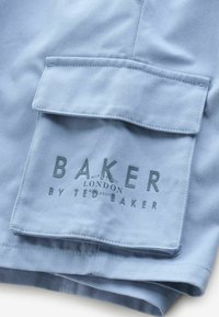 Ljusblå tyghorts med en stor fickklaff som har präglad text "BAKER LONDON BY TED BAKER." Mjuk textur med subtila sömdetaljer.