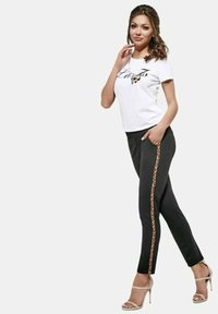 Czarne spodnie z lampasami w panterkę i biały T-shirt z grafiką, zestawione z cielistymi sandałami na wysokim obcasie.