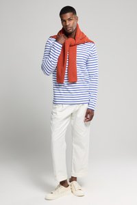 Blauw-wit gestreepte blouse met lange mouwen, oranje gebreide sjaal om de nek, witte broek met manchet en beige sneakers.