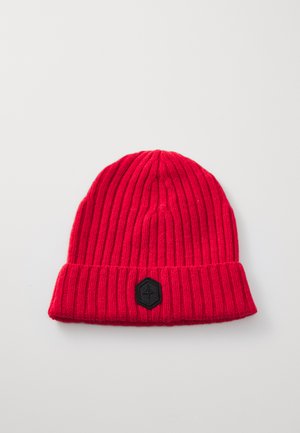 Un bonnet en tricot rouge avec une texture côtelée et un revers. Il présente un patch hexagonal noir à l'avant.