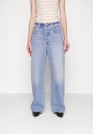 Jeans a gamba larga di un blu chiaro con una finitura sbiadita, design a cinque tasche e orlo grezzo. Abbinati a una canotta beige a righe e scarpe nere.